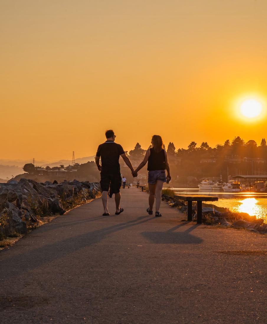 A couple walking hand in hand by the water at sunset