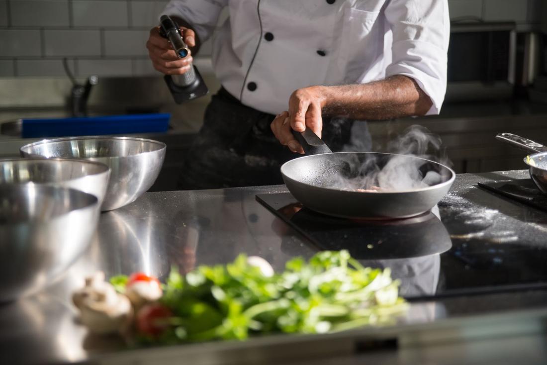 A chef cooking at a steel kitchen counter