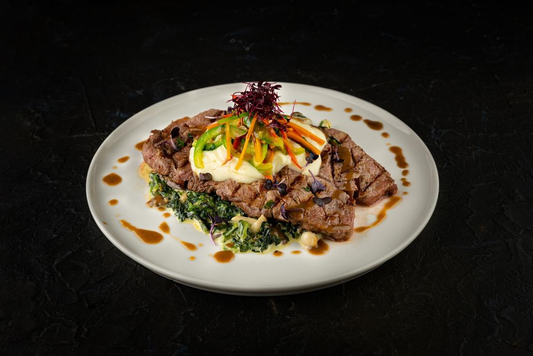 A plated steak with greens and sauce